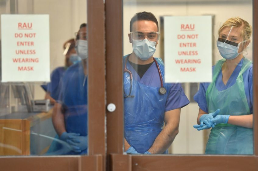 photo shows nurses in PPE standing behind a hospital door with a sign saying 'Do not enter unless wearing mask'.
