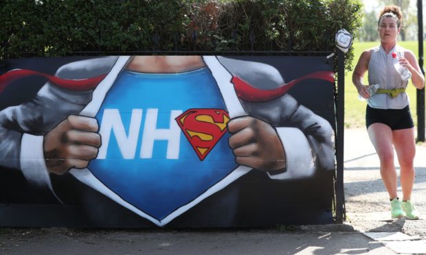 A runner passes street art in appreciation of the NHS placed near to the Francis Drake Bowls Club in Hilly Fields Park, in Lewisham.