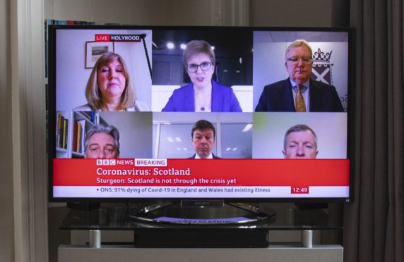 Scotland's First Minister Nicola Sturgeon and other party leaders are seen on television in a living room during the broadcast of a "virtual" session of First Minister's Questions.