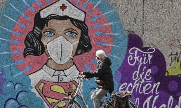 A woman on a bicycle passes a coronavirus graffiti by street artist 'Uzey' showing a nurse as Superwoman, the lettering reads "for the real heroes" on a wall in Hamm, Germany,