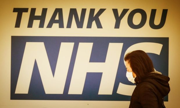 People with masks walk past signage thanking NHS workers in Dundee during the lockdown.