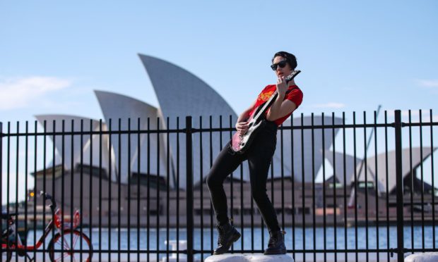 A young woman performs guitar near the Sydney Opera House in Sydney, Australia