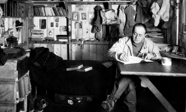 Captain Robert Falcon Scott writing at a table in his quarters (known as his 'den') at the British base camp in Antarctica.
