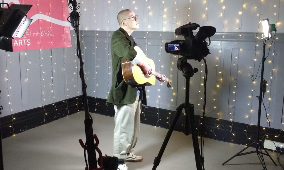 Blair Davie performing in front of camera on tripod in room bedecked in fairy lights