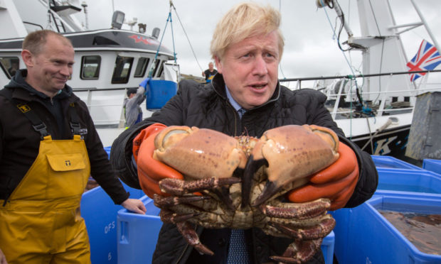 Prime Minister Boris Johnson holds crabs caught on the Carvela with Karl Adamson at Stromness Harbour during a visit to Scotland.
