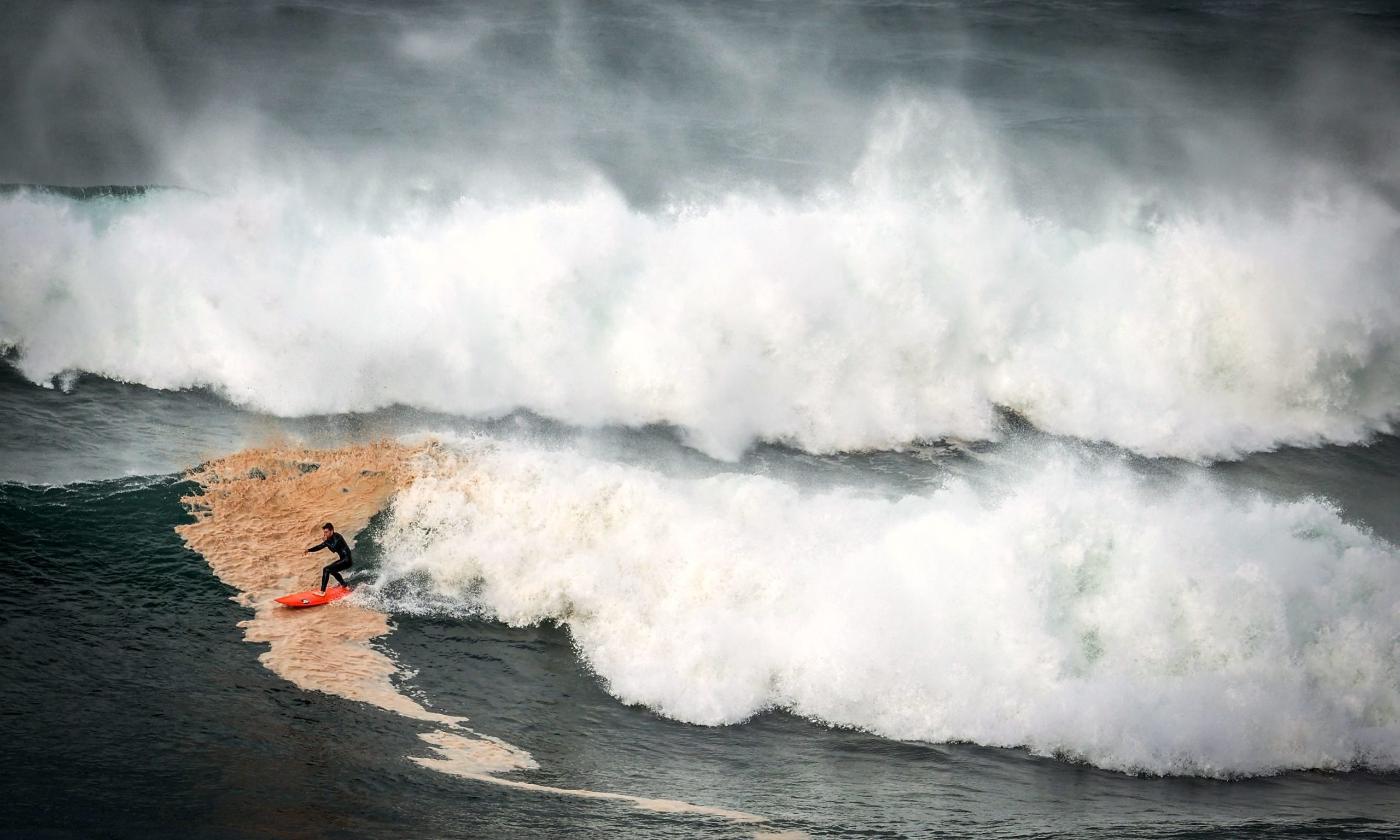 A surfer rides a large wave at Warriewood Beach during a stormy day.