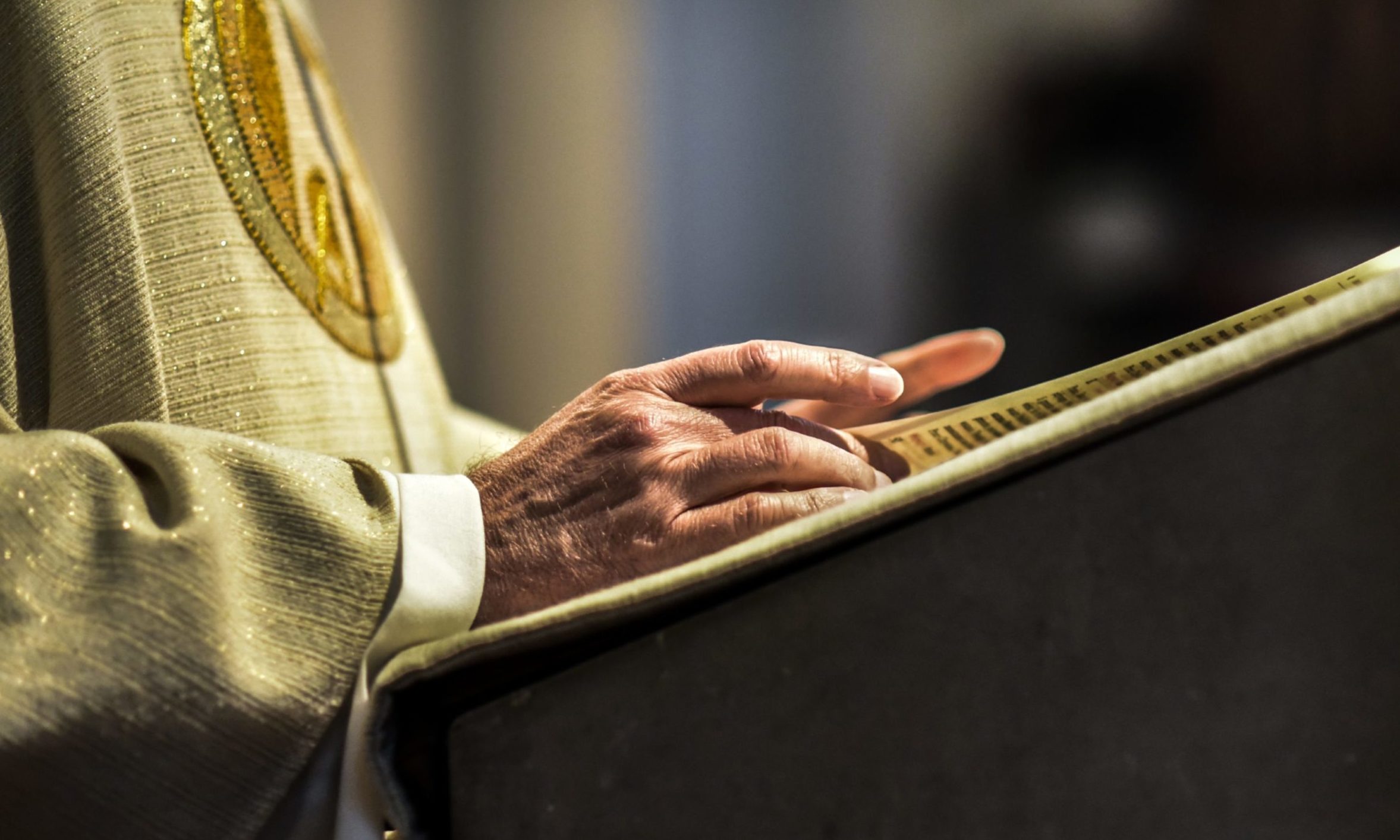 The hands of a catholic priest reading a bible.