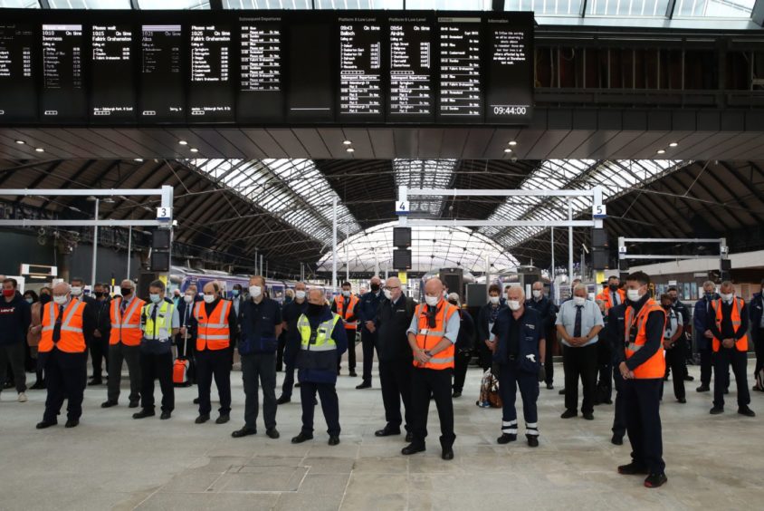 Members of the public join rail staff as they stand in Glasgow Queen Street Station.