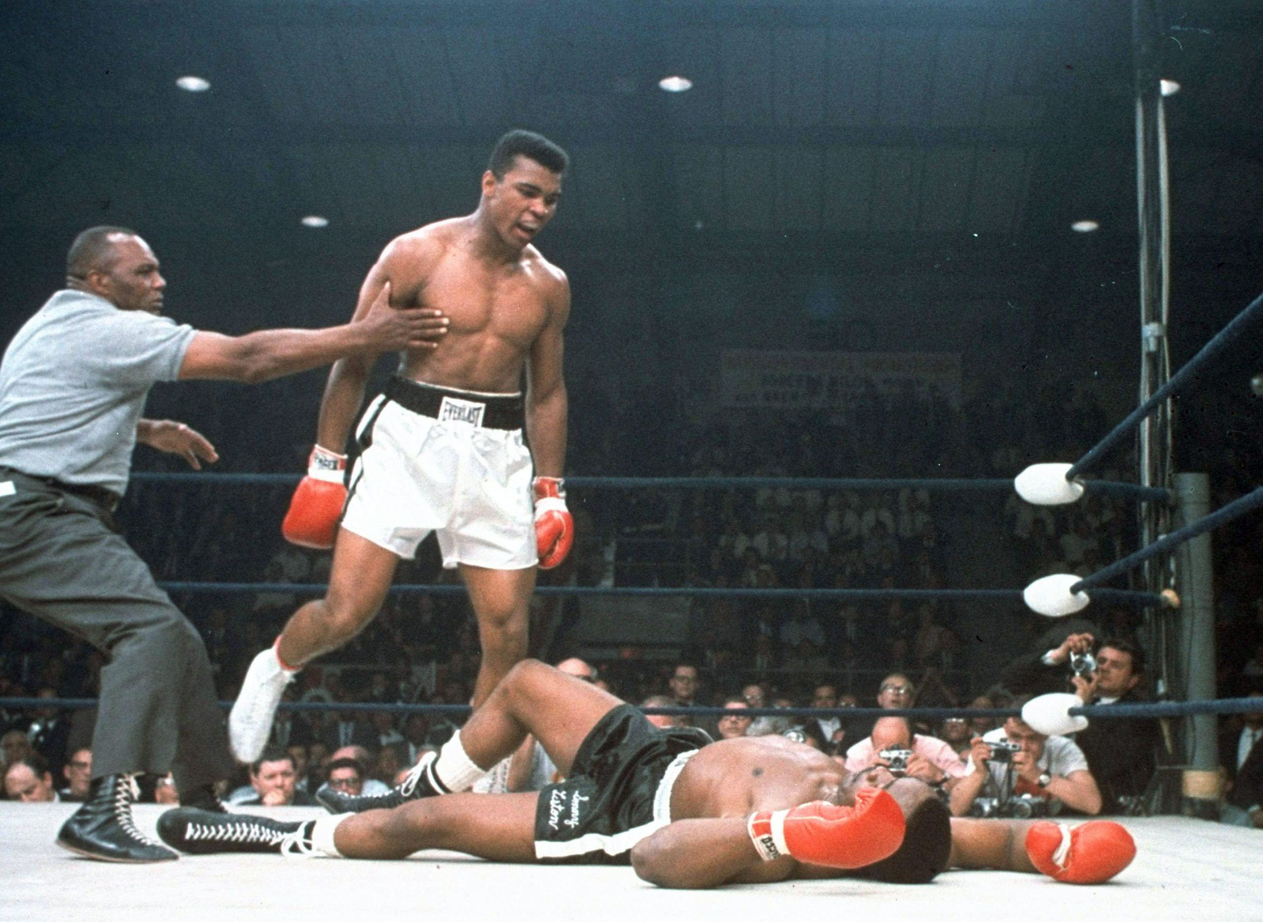 Muhammad Ali is held back by referee Joe Walcott, left, after Ali knocked out Sonny Liston in the first round of their 1965 title fight in Lewiston, Maine.
