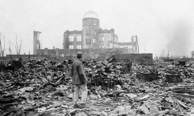 An allied correspondent standing in the rubble in front of the shell of a building that once was a movie theatre in Hiroshima, Japan, a month after the first atomic bomb ever used in warfare was dropped by the US on Monday, August 6, 1945.