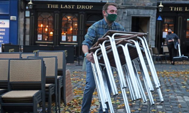 A man stacks away chairs outside The Last Drop pub as it closes in The Grassmarket, Edinburgh, after temporary restrictions announced by First Minister Nicola Sturgeon to help curb the spread of coronavirus.