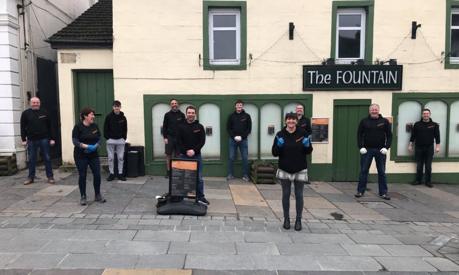 Group of people, standing metres apart from one another outside the Fountain bar in Aberfeldy during the Covid lockdown