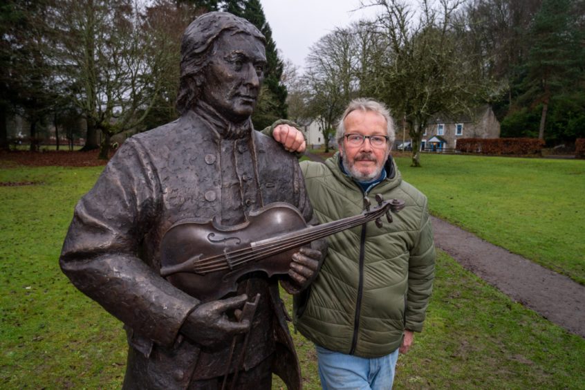 Pete Clark leaning next to bronze statue of Niel Gow holding a fiddle