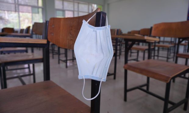 The used medical face mask hangs on the wood lecture chairs in the empty classroom. Concept during the coronavirus outbreak.
