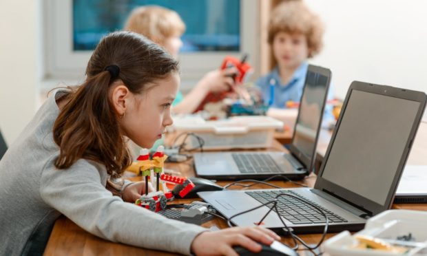 Girl using a laptop while assembling a robot from plastic bricks. STEM Education for kids.; Shutterstock ID 1187282503