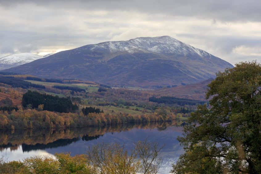 View over Loch Tummel and trees in autumn colour towards the snow capped peak of Schiehallion mountain.