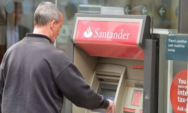 A man using a cash machine outside a branch of Santander.