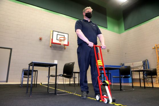 Head caretaker Brian Smith puts down the social distance tape in the gym hall.