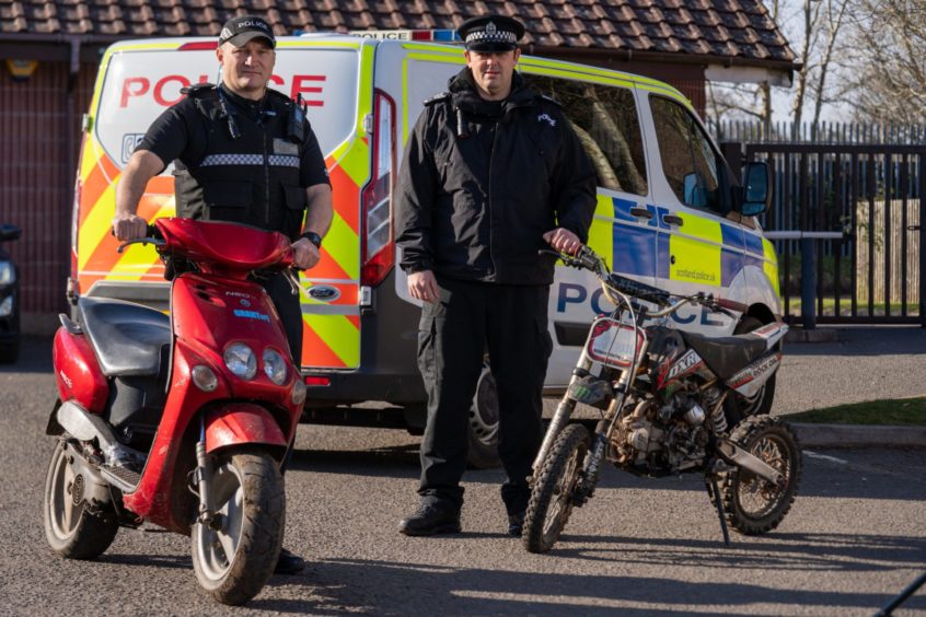 Two police officers standing with off-road bikes and scooters they have seized in Dundee