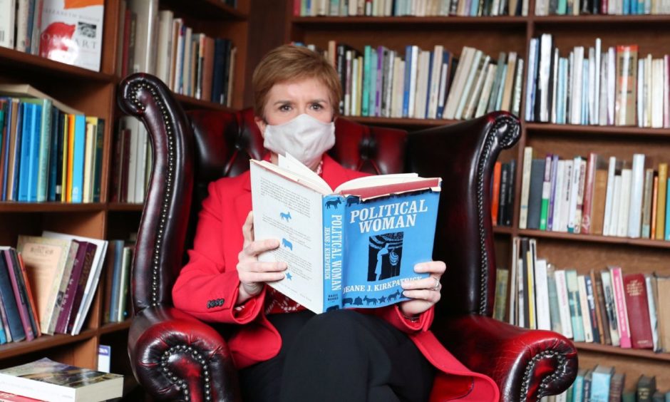 Nicola Sturgeon in front of book shelves, holding a book titled Political Woman.