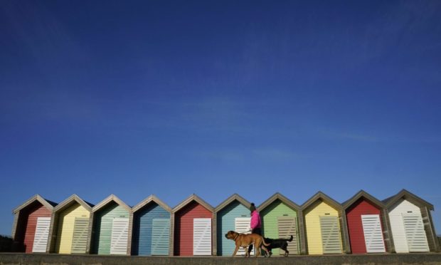 A woman walks her dog past beach huts at Blyth beach in Northumberland in the cold. Picture date: Wednesday April 7, 2021. PA Photo. Photo credit should read: Owen Humphreys/PA Wire