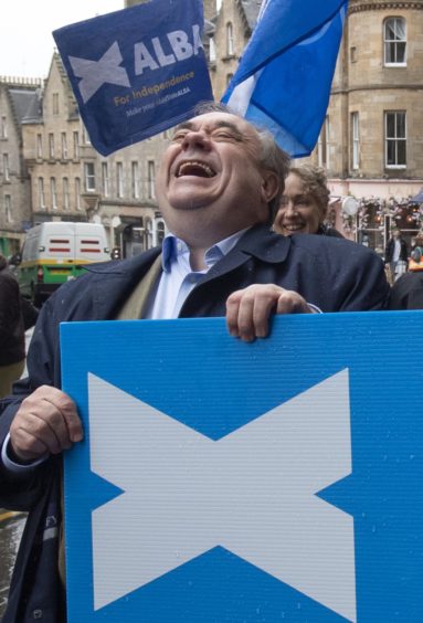 Alex Salmond laughing behind an Alba Party placard.