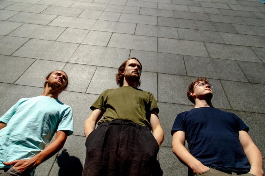 The band The Fergus McCreadie Trio posing in front of a stone wall