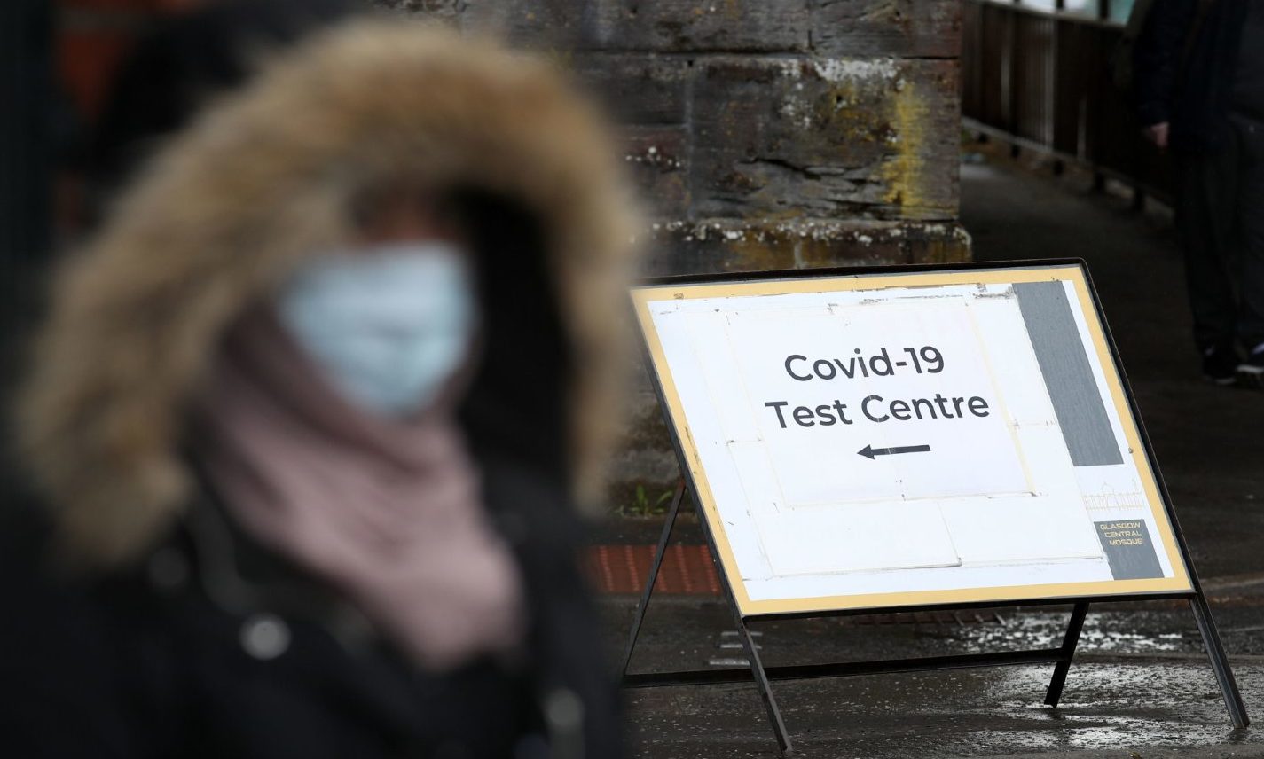A person wearing a mask walking next to a Covid-19 Test Centre sign