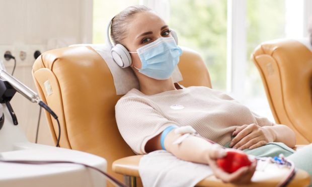 A woman lying down giving blood wearing a mask