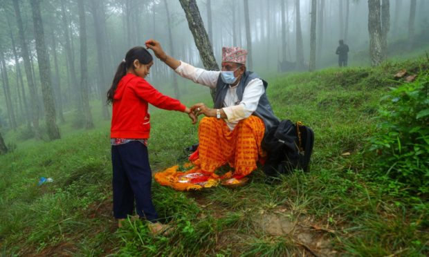 A priest ties thread on the hand of a girl and offers tika on the forehead at a religious site in Kavre of Nepal on the occassion of Janai Purnima.
Nepal celebrates Festival of Threads, Kavre, Nepal. Photo by Subash Shrestha/Shutterstock