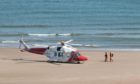 A coastguard helicopter with a paramedic on board waits on the beach at Lunan Bay in July
