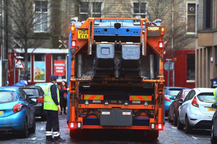 A refuse worker putting bins into the back of a bin lorry on a Dundee street