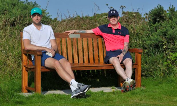 Two passing golfers resting on the Graham Proctor memorial bench at St Andrews Links