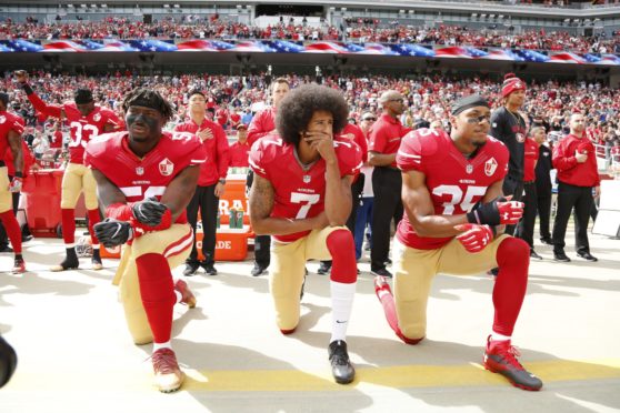 San Francisco 49ers quarterback Colin Kaepernick (c) along with Eli Harold (l) Eric Reid (r) take a knee during the US national anthem.
