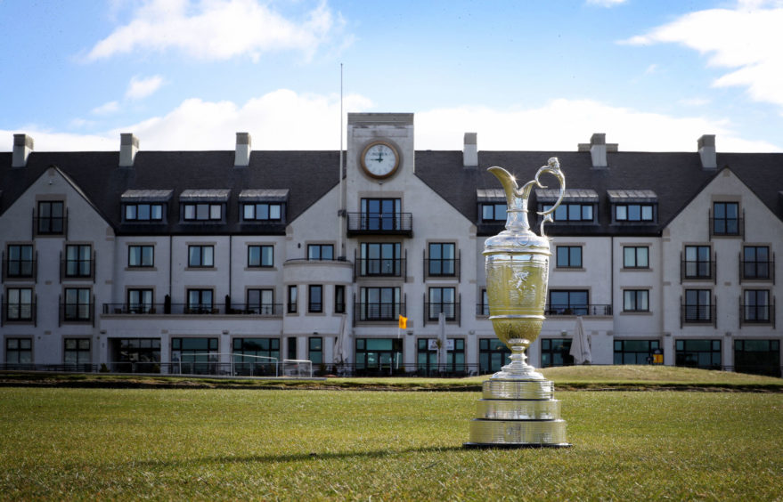 The Claret Jug trophy in front of the imposing white clubhouse at Carnoustie Golf Links course.