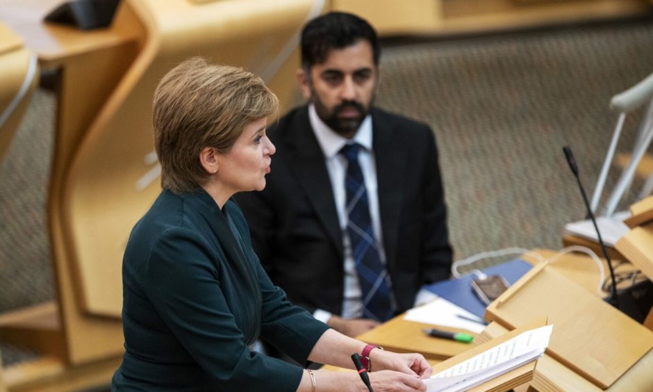 Former First Minister of Scotland Nicola Sturgeon speaking in the Scottish Parliament debating chamber while Humza Yousaf stares into the middle distance by her side.