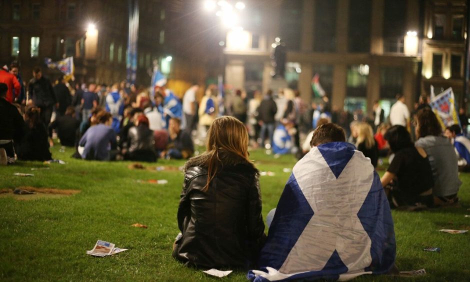 People with Scotland flags seated and standing in groups across George Square in Glasgow on the night of the Scottish independence referendum in 2014.
