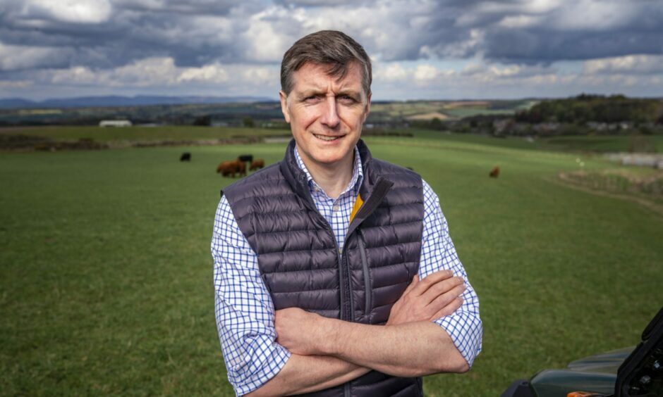 Simon Howie, arms folded, standing in a field in Perthshire