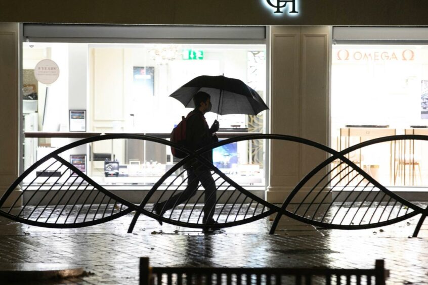 A person walking through Dundee city centre at night with an umbrella.