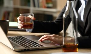 A person drinking at their work desk. Image: Shutterstock.