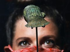 A gallery assistant looks at a socketed axe on display during a preview of the Havering Hoard: A Bronze Age Mystery exhibition at the Museum of London Docklands (Aaron Chown/PA)