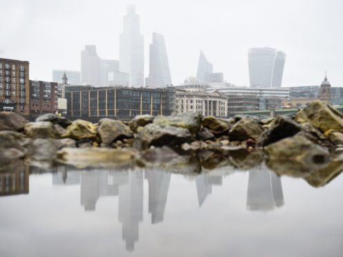The City of London skyline is reflected in a puddle on the banks of the River Thames in London (Kirsty O’Connor/PA)