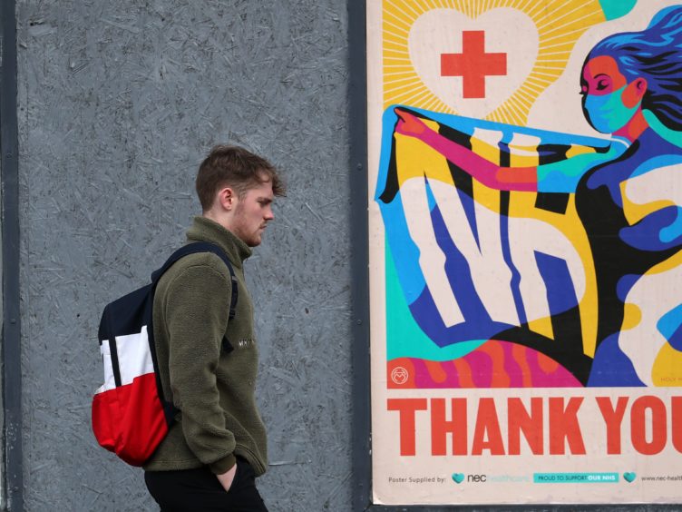 A person walks passed an advertising board in Glasgow showing a Thank You NHS poster (Andrew Milligan/PA)