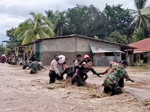 Soldiers and police officers assist residents to cross a flooded road in Indonesia (AP)