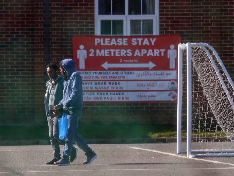 Two men walk past signs recently erected at Napier Barracks in Folkestone, Kent (PA)