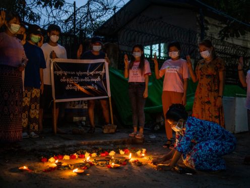 A woman lights a candle while others flash the three-fingered sign of resistance during a candlelight vigil to remember those who died in the military junta’s violent response to anti-coup demonstrations in Yangon, Myanmar (AP)