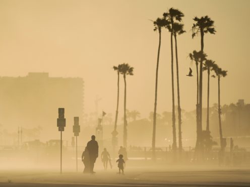 People walk and skateboard on a beach path as evening winds kick up sand in Long Beach, California (Ashley Landis/AP)
