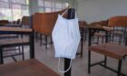 The used medical face mask hangs on the wood lecture chairs in the empty classroom. Concept during the coronavirus outbreak.