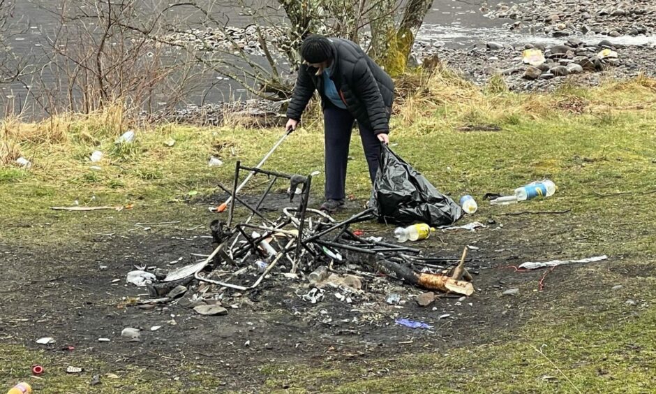 person picking up rubbish from a camp fire left behind by dirty campers