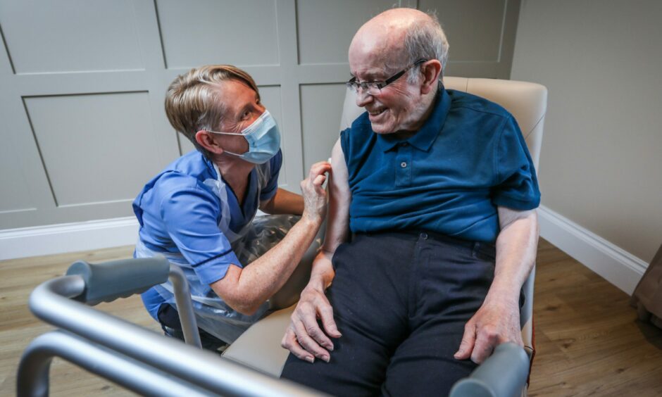 An elderly man sitting in a seat receiving a Covid vaccine jab